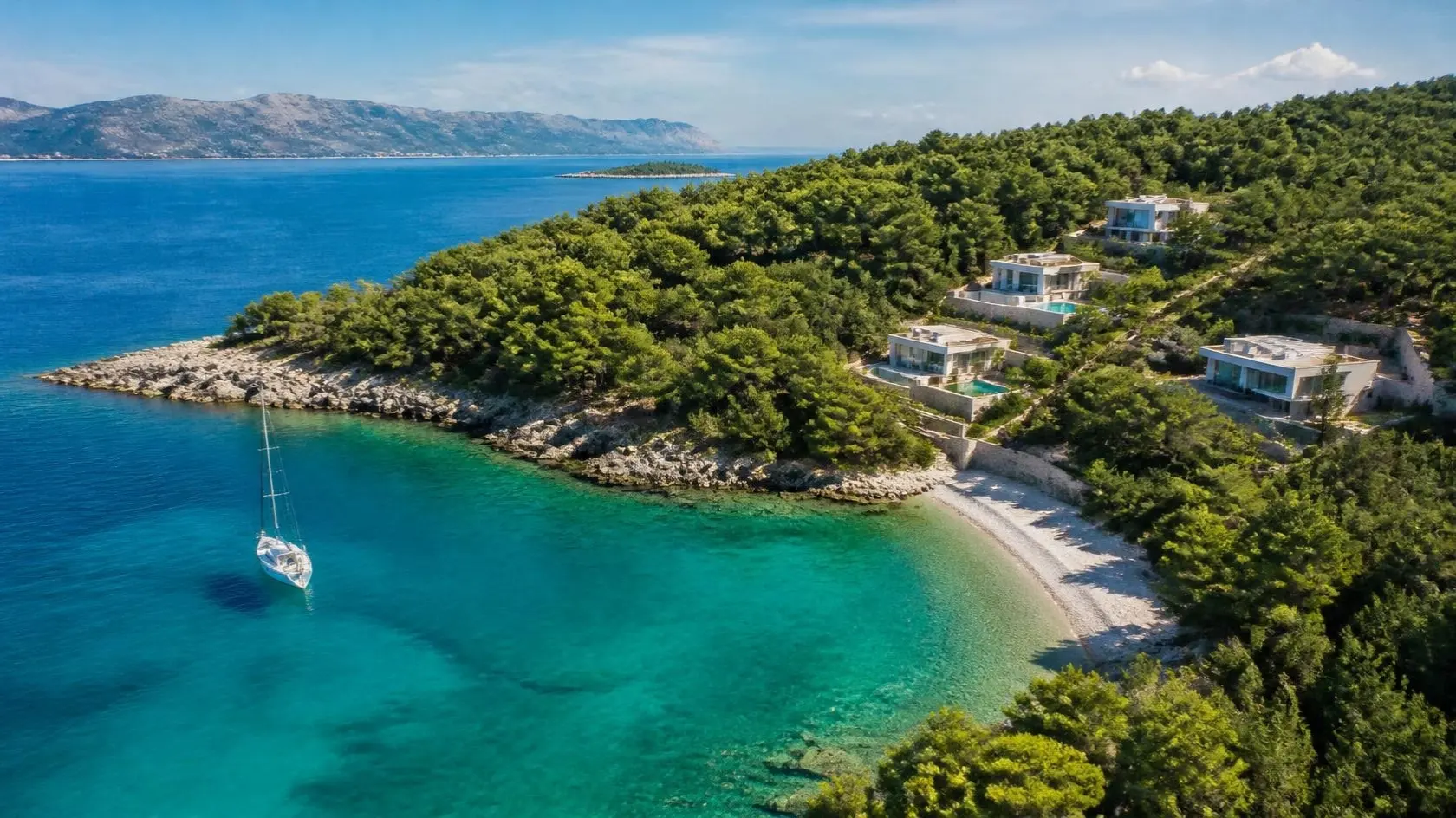 Luftbild einer türkisfarbenen Inselbucht mit Pinienwald, Kiesstrand und modernen Villen