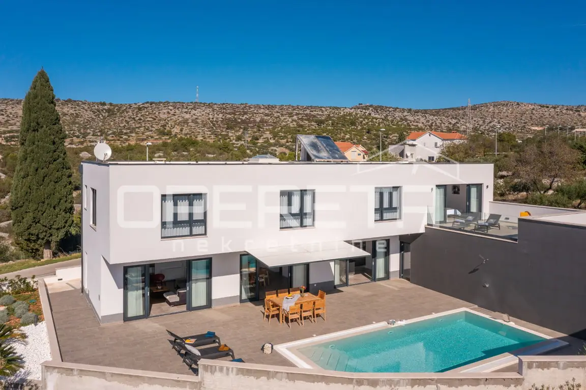 Die Villa mit Pool und Terrassen von oben, dahinter Hügel und Dorf