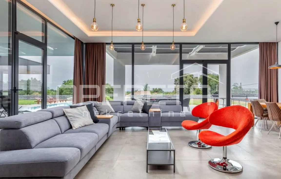 Wohnzimmer mit grauem Sofa, roten Sesseln und raumhohen Fenstern