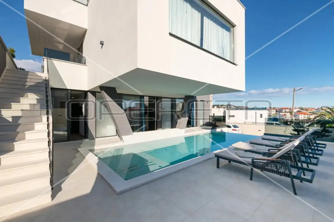 Pool mit Liegen vor der weißen Fassade und Außentreppe der Villa